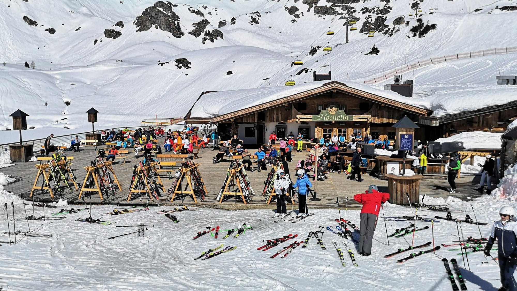 Skifahrer sitzen in Österreich während einer Pause auf der Terrasse einer geschlossenen Skihütte unter Berücksichtigung eines coronabedingten Mindestabstands.