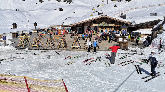 Skifahrer sitzen in Österreich während einer Pause auf der Terrasse einer geschlossenen Skihütte unter Berücksichtigung eines coronabedingten Mindestabstands.&nbsp;