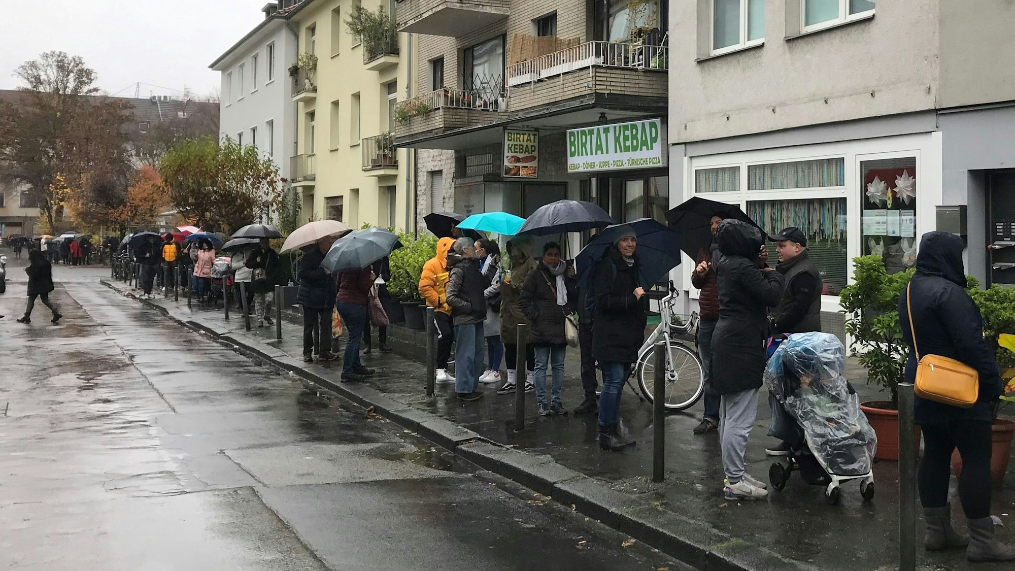 Menschen stehen mit Regenschirmen Schlange.