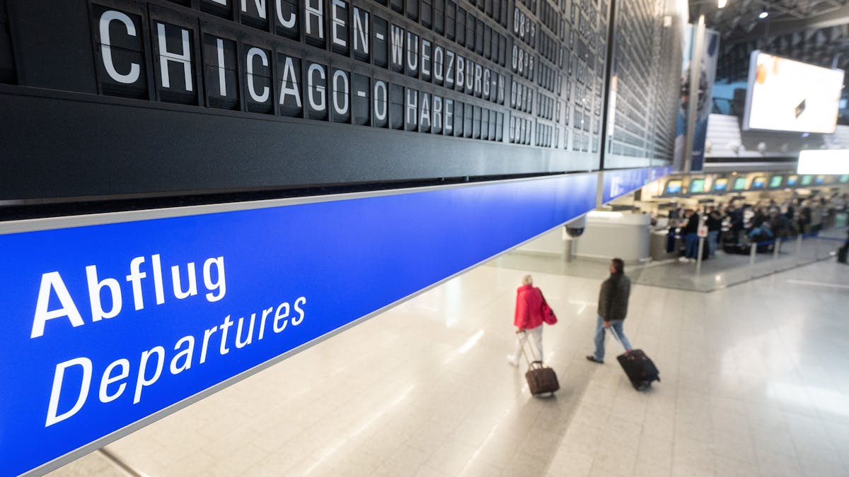 Ein Flug nach Chicago O·Hare in den USA wird auf dem Flughafen Frankfurt auf einer Tafel angezeigt unter der Passagiere mit Koffern entlang gehen.
