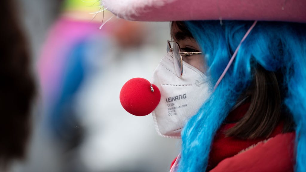 Eine verkleidete Frau trägt eine Clownsnase über einer FFP2 Maske.&nbsp;