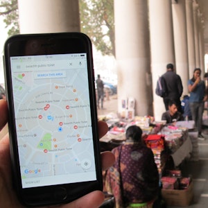 Das Symbolfoto (aufgenommen am 23. Dezember 2016 in Neu Delhi) zeigt ein Handy mit geöffnetem Google Maps, im Hintergrund sieht man den Connaught Place.