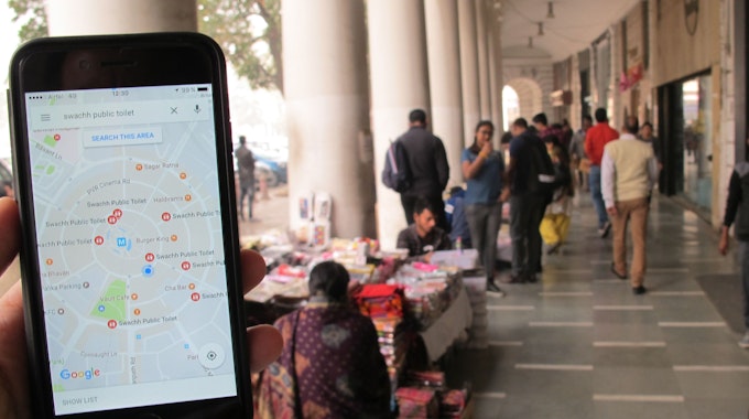 Das Symbolfoto (aufgenommen am 23. Dezember 2016 in Neu Delhi) zeigt ein Handy mit geöffnetem Google Maps, im Hintergrund sieht man den Connaught Place.
