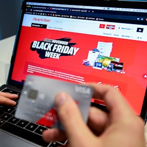 Eine Person hält eine Kreditkarte, während auf einem Laptop zu lesen ist „Black November. Black Friday Woche“.