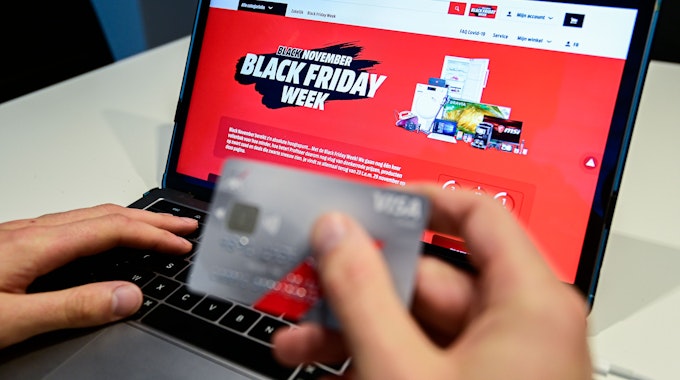 Eine Person hält eine Kreditkarte, während auf einem Laptop zu lesen ist „Black November. Black Friday Woche“.