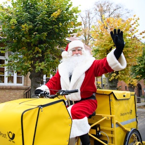 Der Weihnachtsmann sitzt nach seiner Ankunft am Weihnachtspostamt winkend auf dem Fahrrad.