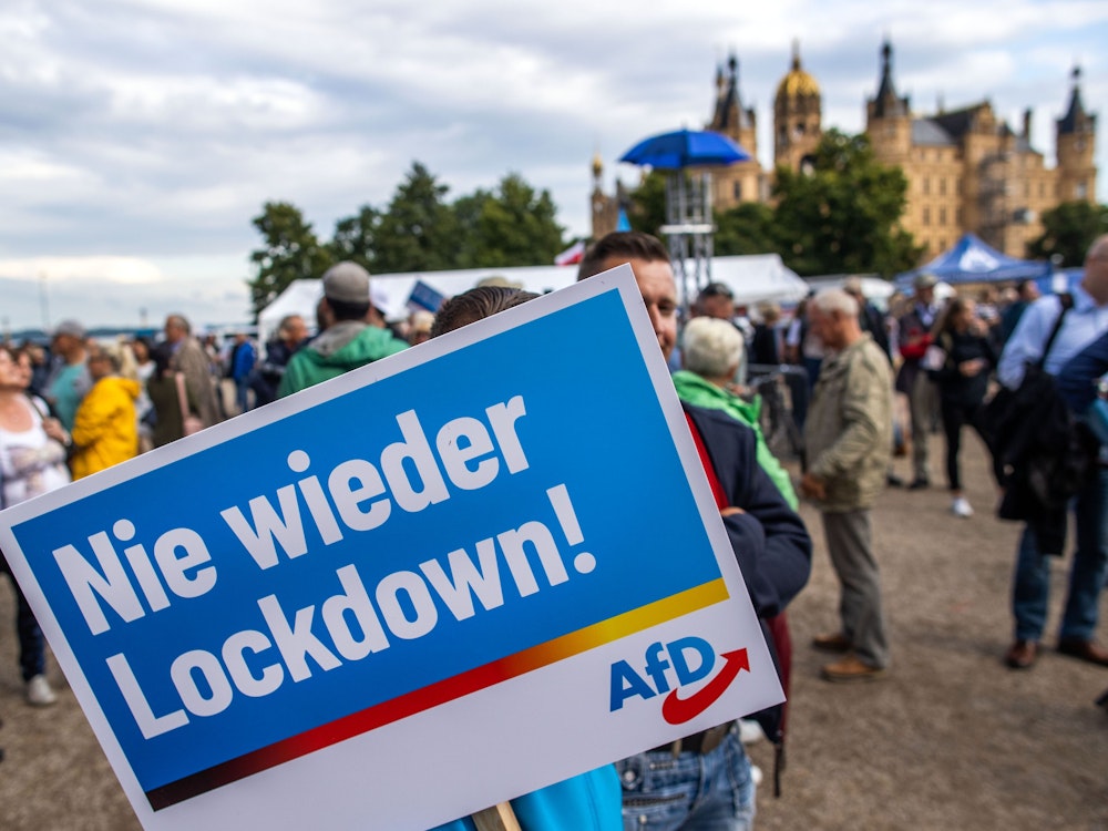 Ein Anhänger der AfD steht mit einem Plakat mit der Aufschrift „Nie wieder Lockdown“ zum Auftakt der Wahlkampftour der AfD vor dem Schweriner Schloss.