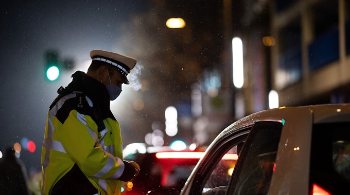 Das Symbolbild zeigt einen Polizeibeamten, der während einer Verkehrskontrolle mit einem Autofahrer spricht. In Köln haben vier junge Männer mit einer Luftdruckpistole auf Passanten geschossen.