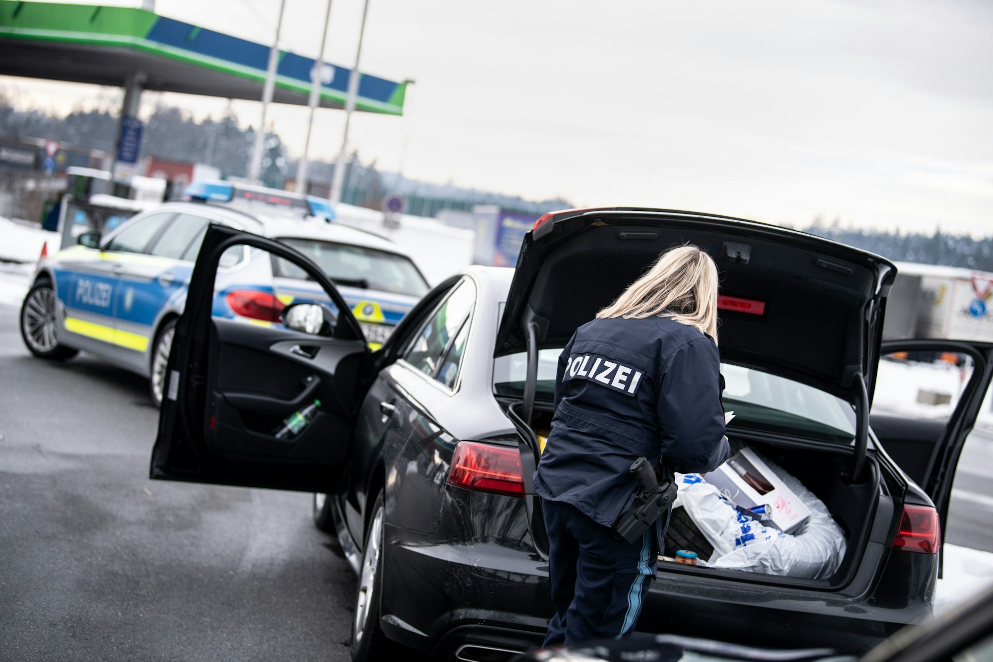 Eine Polizistin kontrolliert auf einem Rastplatz den Kofferraum eines Fahrzeugs.