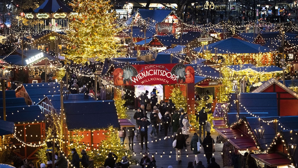 Menschen besuchen den Weihnachtsmarkt „Wienachtsdorf“ auf dem Zürcher Sechseläutenplatz.