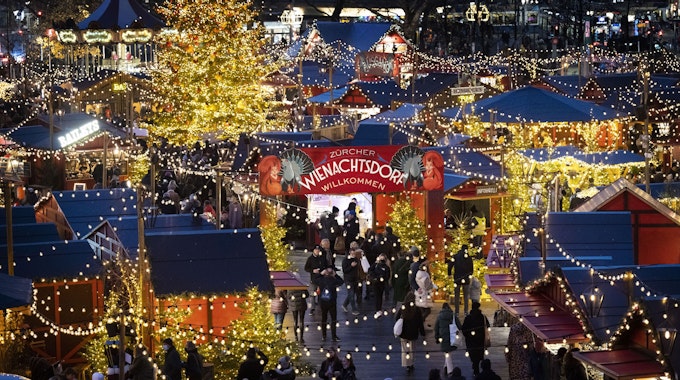 Menschen besuchen den Weihnachtsmarkt „Wienachtsdorf“ auf dem Zürcher Sechseläutenplatz.