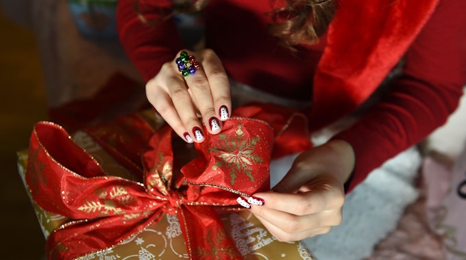 Auf dem Foto sieht man die Hände einer jungen Frau und ein großes Weihnachtsgeschenk.