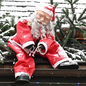 Eine Weihnachtsmannfigur hängt als Dekoration an einem Dach.