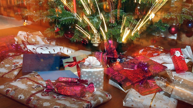 Verpackte Weihnachtsgeschenke liegen unter einem Christbaum.