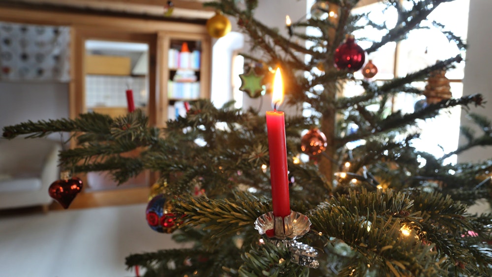 Eine Kerze brennt an einem geschmückten Weihnachtsbaum.