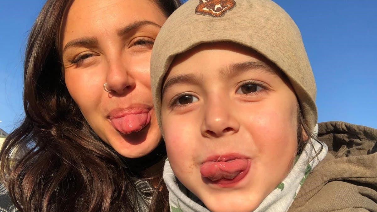Eine junge Mutter und ihr Sohn albern vor der Fotokamera, strecken dem Fotografen die Zunge raus.