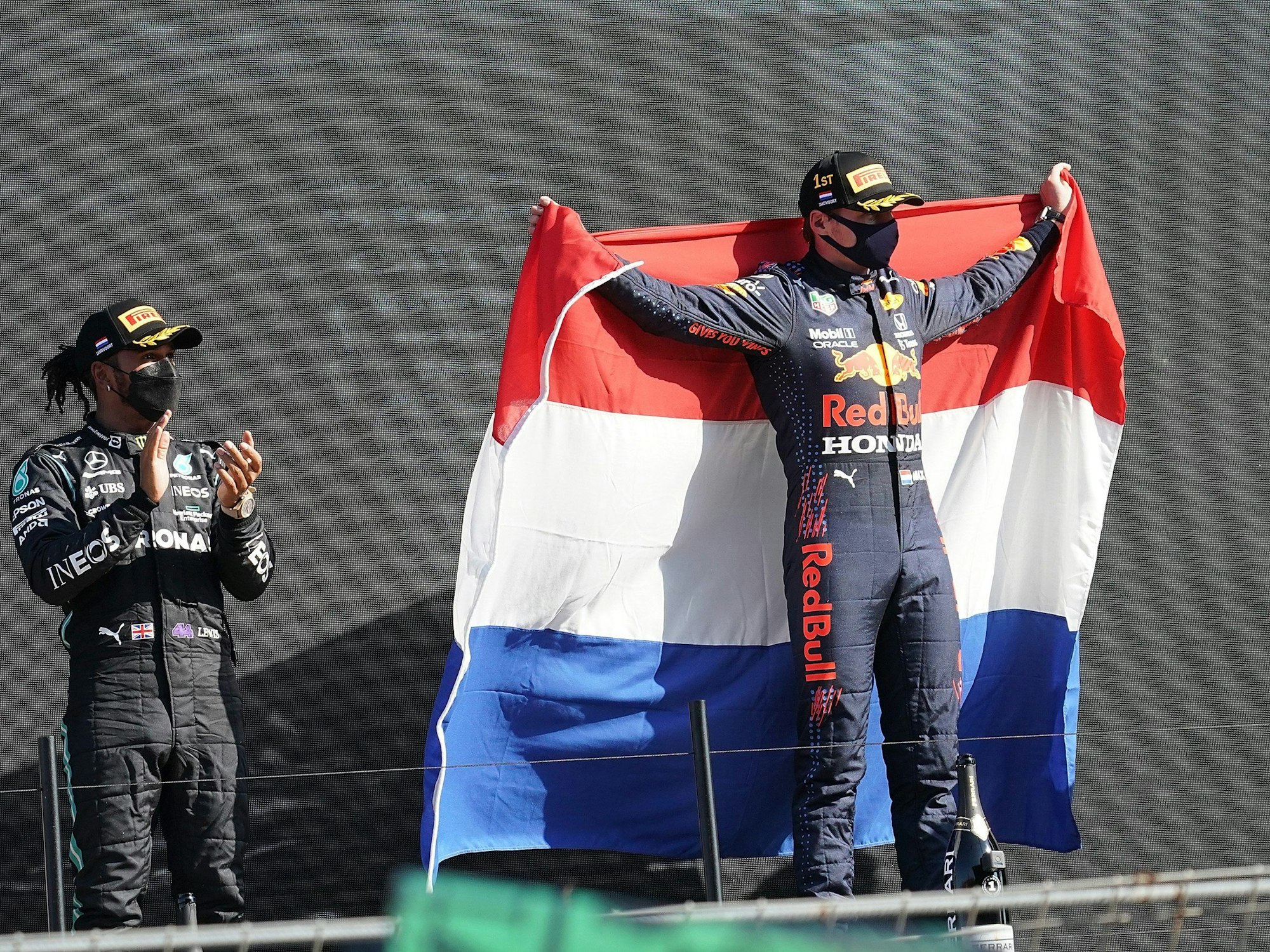 Der Zweitplatzierte Lewis Hamilton (l) aus Großbritannien vom Team Mercedes-AMG Petronas Formula One Team applaudiert während der Sieger Max Verstappen aus den Niederlanden vom Team Red Bull Racing Honda eine niederländische Fahne hält.