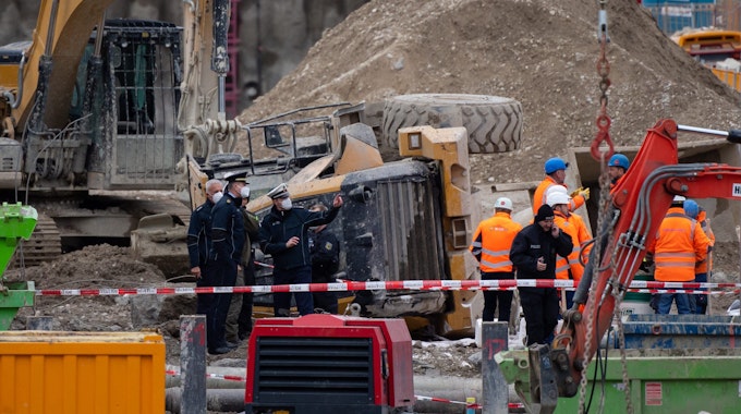 Polizisten und Bahnbedienstete stehen auf einer Baustelle auf einem Bahngelände an der Donnersbergerbrücke neben einem umgestürzten Radlader. Bei der Explosion einer Fliegerbombe aus dem Zweiten Weltkrieg sind an der Bahnstrecke zum Hauptbahnhof in München mehrere Menschen verletzt worden.