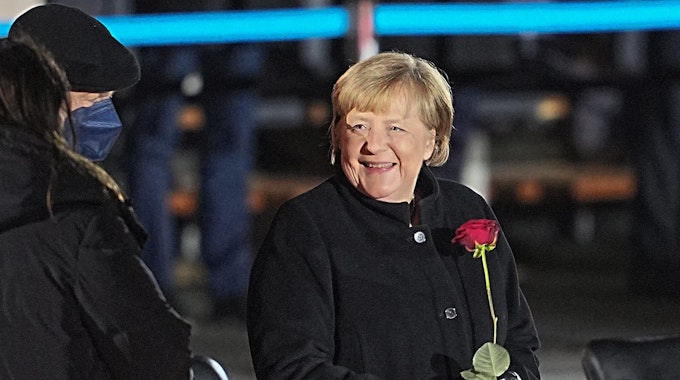 Bundeskanzlerin Angela Merkel lacht nach ihrer Verabschiedung durch die Bundeswehr (Foto: 2. Dezember 2021) mit einer Rosen in der Hand neben ihrem Mann, Joachim Sauer.