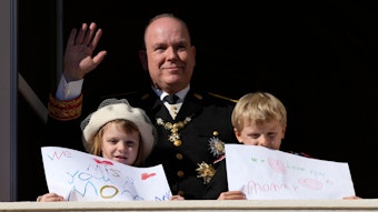Fürst Albert II. von Monaco (M) winkt während der Feierlichkeiten zum Nationalfeiertag vom Balkon des Palastes von Monaco, während seine Kinder Fürst Jacques und Prinzessin Gabriella von Monaco Bilder mit Botschaften für ihre Mutter Fürstin Charlène in der Hand halten.