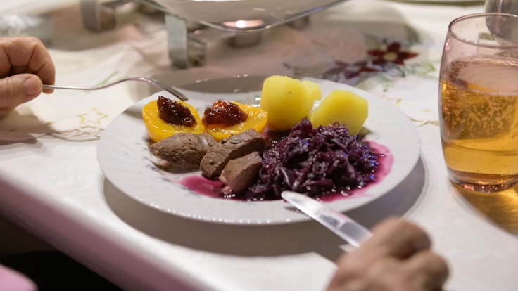 Damhirsch-Rücken mit Kartoffeln und Rotkohl sowie Preiselbeergelee auf Aprikosen liegen verzehrfertig auf einem Teller an Heiligabend.