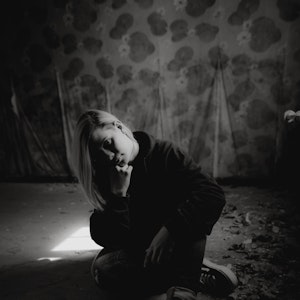 Katha Rosa sitzt auf dem Boden und hat das Kinn auf die rechte Hand gestützt. Das Foto ist schwarz weiß.