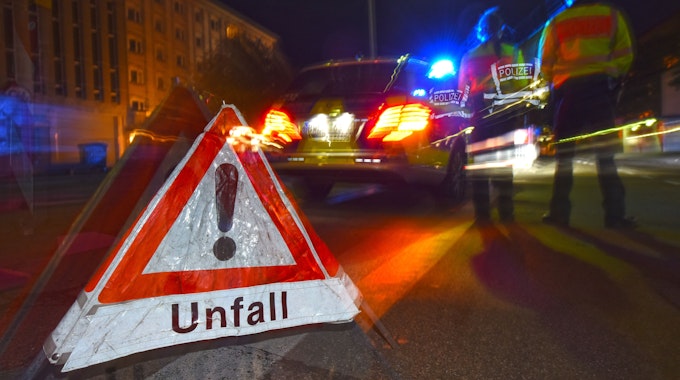 Ein Polizeifahrzeug steht mit Blaulicht auf der Straße. Daneben steht ein Warndreieck mit dem Schriftzug „Unfall“.