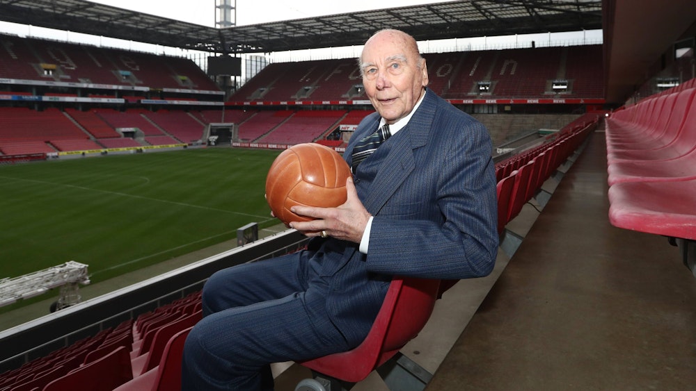 Horst Eckel sitzt mit einem alten Fußball im Stadion.