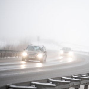 Autos fahren an einem Verkehrsschild vorbei, das vor Schneeglätte warnt.