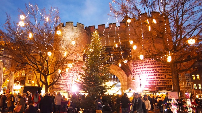 Besucher und Besucherinnen laufen über der Weihnachtsmarkt am Kölner Eigelstein – im Hintergrund die Torburg.