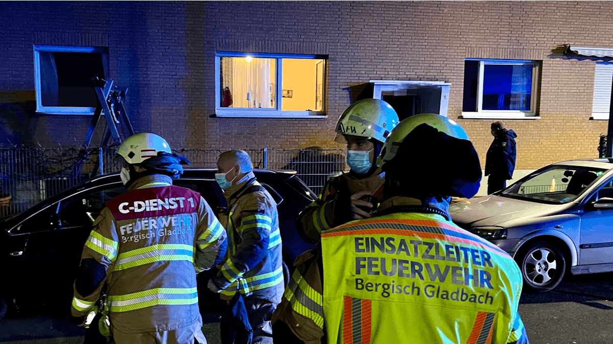 Feuerwehr-Leute stehen auf der Straße vor einem beleuchteten Haus.