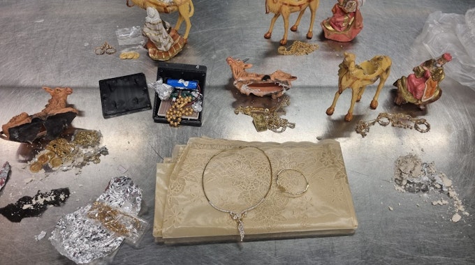 Auf einem Tablett stehen aufgebrochene Krippenfiguren, Goldschmuck und Goldmünzen.