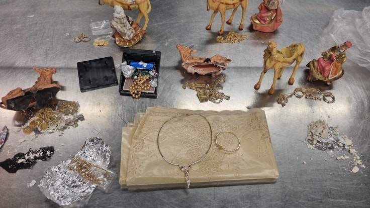 Auf einem Tablett stehen aufgebrochene Krippenfiguren, Goldschmuck und Goldmünzen.