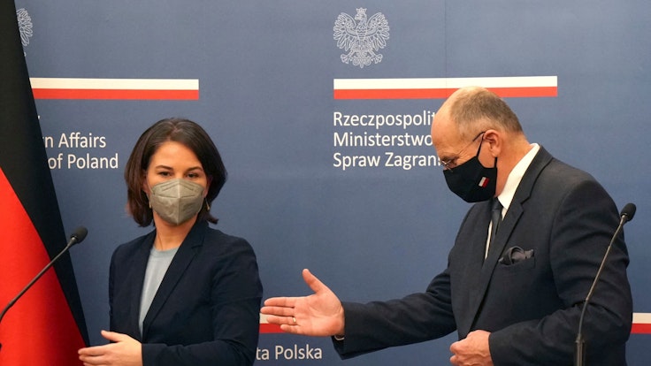 Außenministerin Annalena Baerbock (l.) wir von ihrem polnischen Amtskollegen Zbigniew Rau ans Rednerpult geführt.