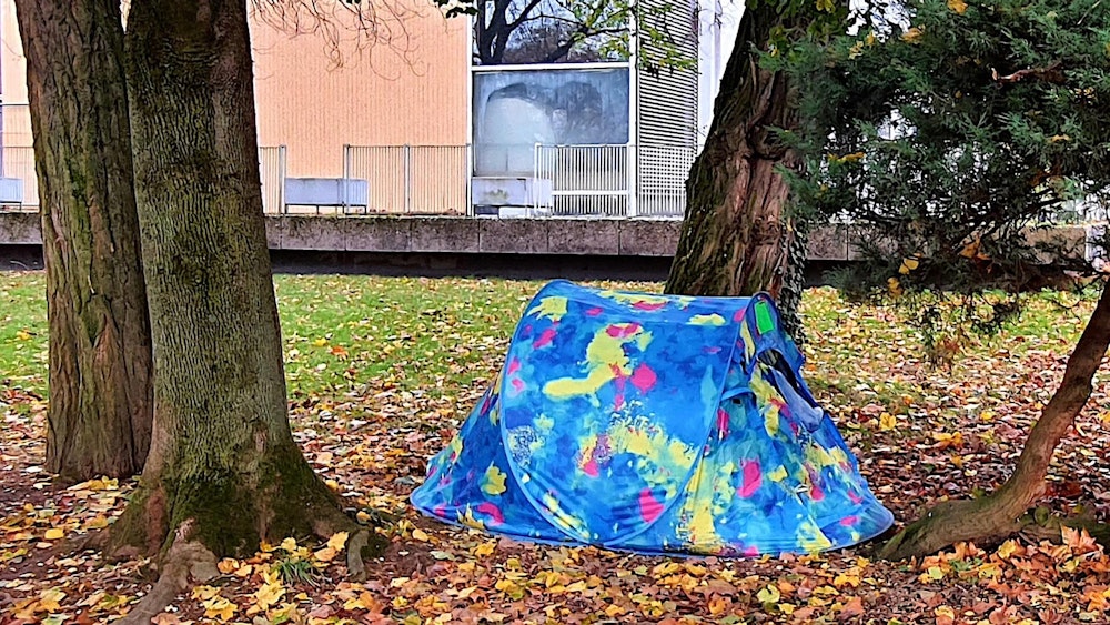 Ein bunt gemustertes Zelt auf einer Wiese zwischen zwei Bäumen.