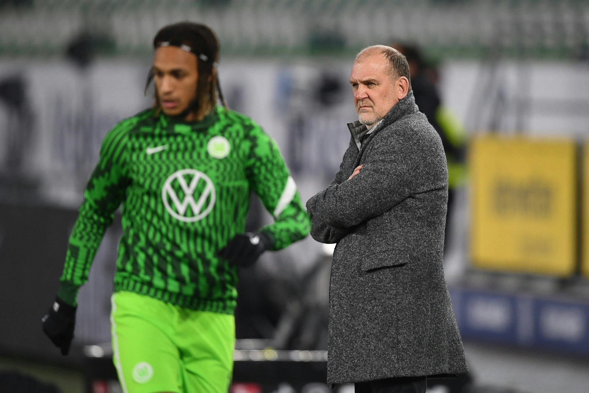 Jörg Schmadtke, Geschäftsführer Sport vom VfL Wolfsburg, im Stadion. Links läuft Wolfsburgs Kevin Mbabu.