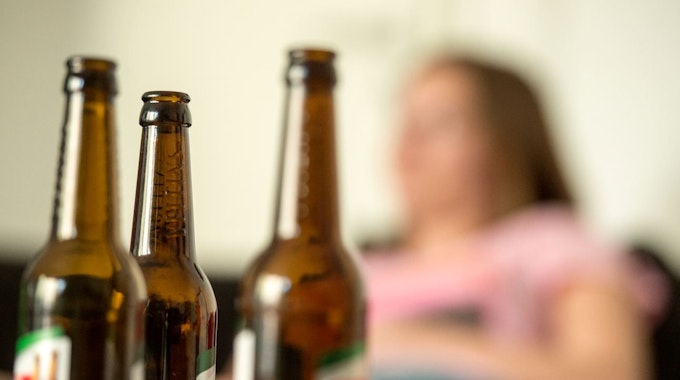 Alkoholsucht ist weiterhin ein großes Problem unserer Gesellschaft. Jetzt erzählt der Ex-Alkoholikerin Nathalie, wie es ihr ergangen ist. Unser Symbolfoto (28. Mai 2016) zeigt eine junge Frau, die hinter leeren Bierflaschen sitzt.