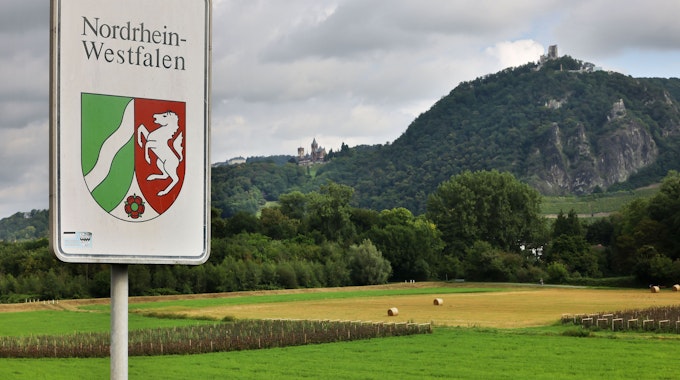 Ein Strassenschild mit dem Landeswappen steht an der Grenze zwischen Nordrhein-Westfalen und Rheinland-Pfalz vor der Kulisse des Drachenfelses.