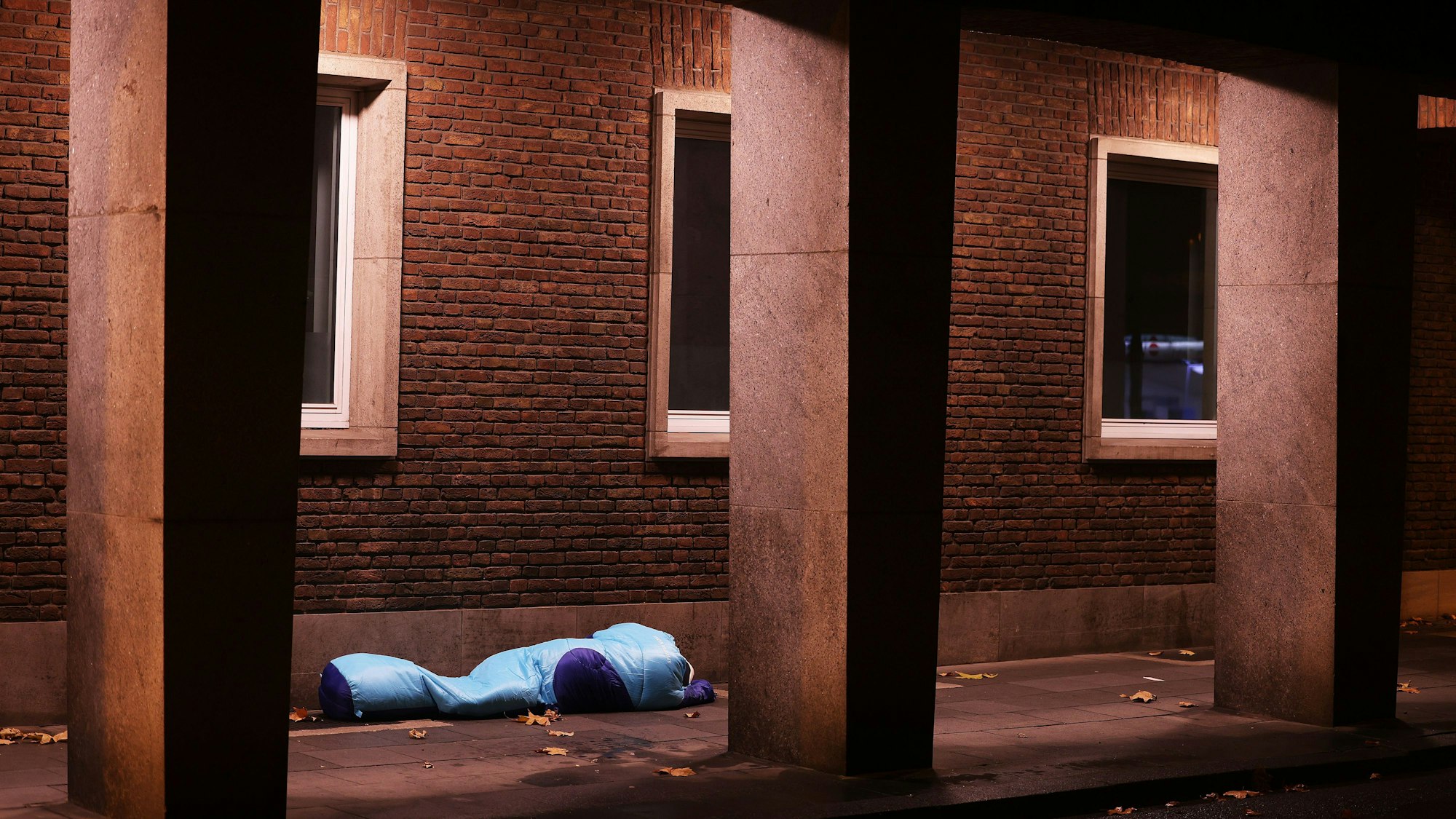 Ein Obdachloser liegt unter einer Überdachung in einer Passage.