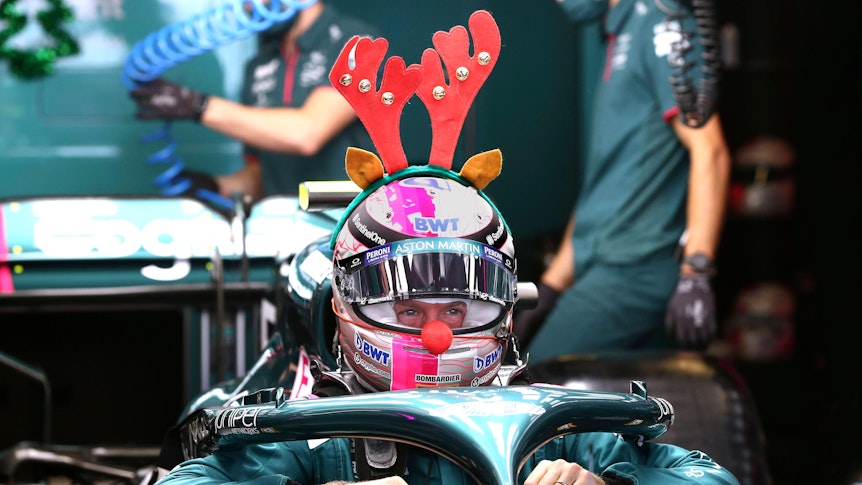 Sebastian Vettel sitzt in seinem Rennwagen. Auf seinem Helm ist ein Geweih platziert und an der Nase trägt er eine rote Plüsch-Nase.