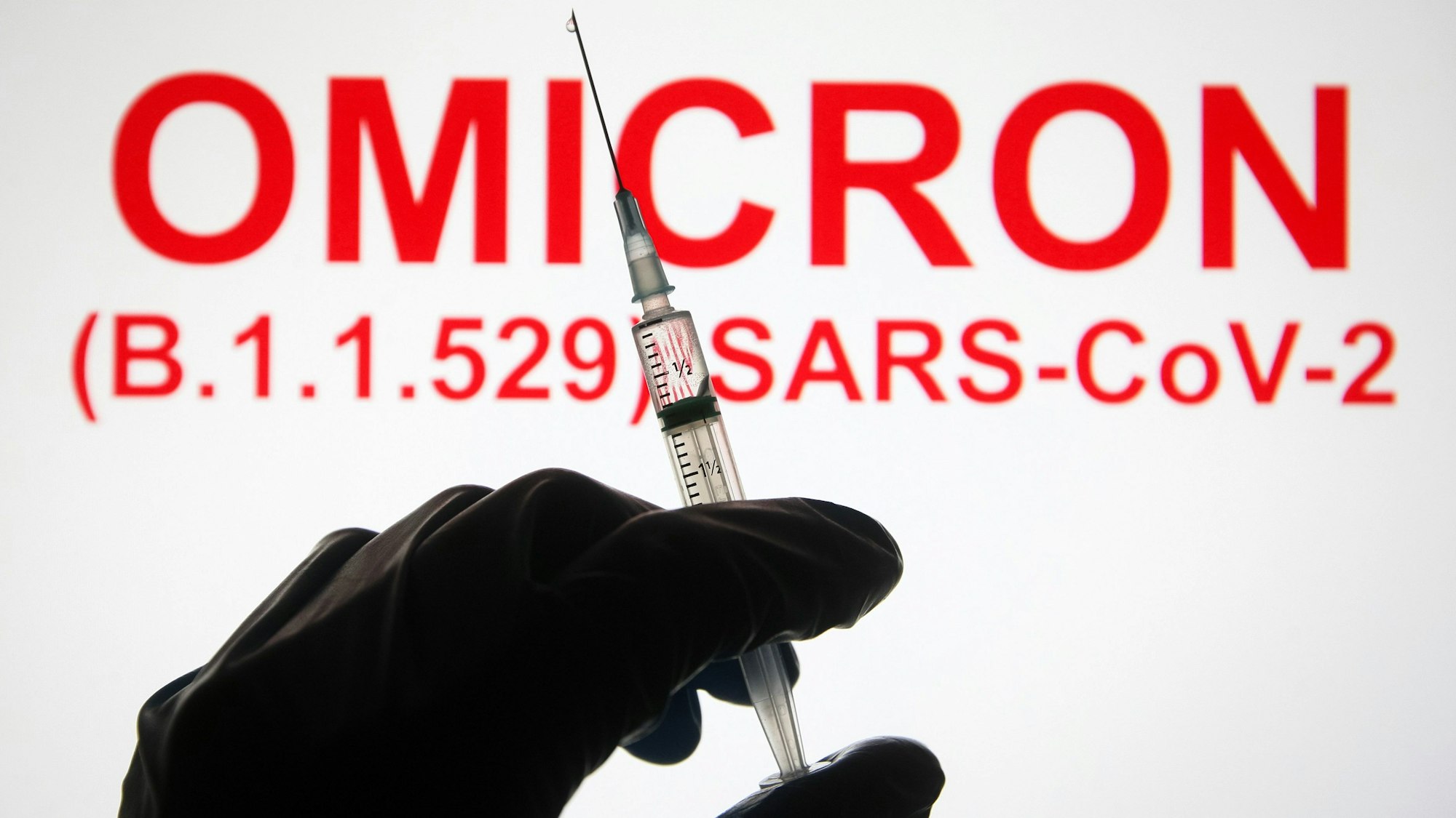 Eine Hand hält vor der Aufschrift „Omicron (B.1.1.529): SARS-CoV-2“ eine Spritze hoch.
