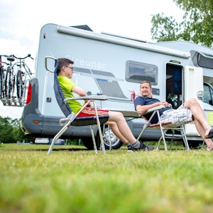 Zwei Männer sitzen auf dem Campingplatz am Birkensee vor ihrem Wohnmobil.