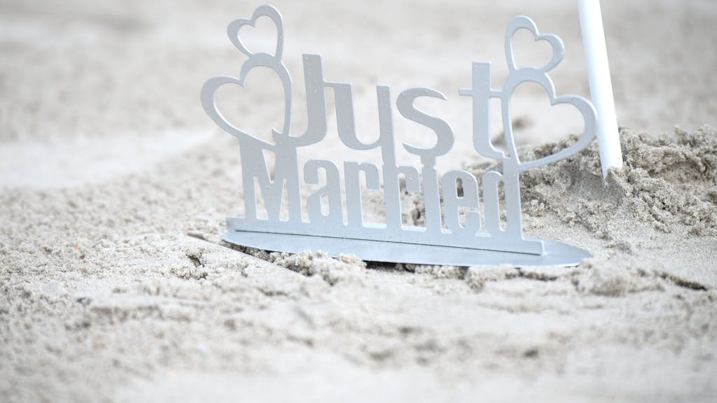 Ein weißer „Just Married“-Metallaufsteller im Sand.