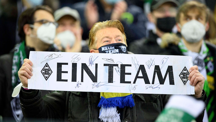 Ein Fan von Fußball-Bundesligist Borussia Mönchengladbach zeigt ein Plakat mit der Aufschrift „Ein Team“. Dieses Foto aus dem Borussia-Park ist am 5. Dezember 2021 entstanden.