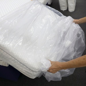 Eine Frau packt in einem Fachgeschäft für Matratzen eine neue Matratze aus der Verpackungsfolie aus.