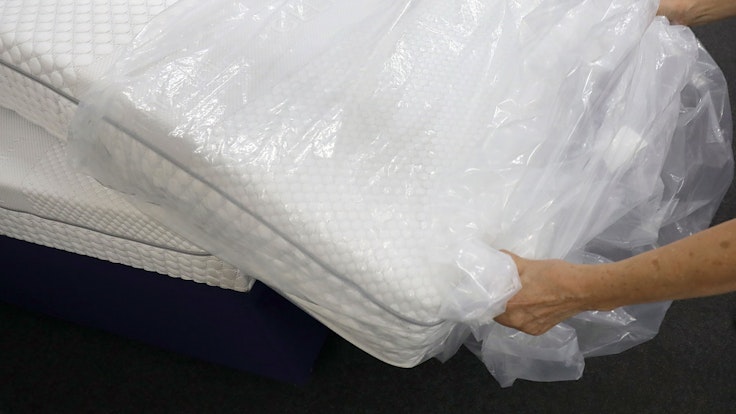 Eine Frau packt in einem Fachgeschäft für Matratzen eine neue Matratze aus der Verpackungsfolie aus.