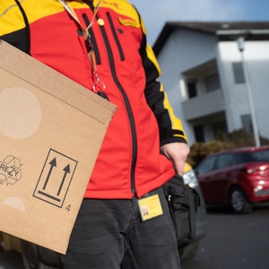 Das Bild zeigt einen DHL-Mitarbeiter mit einem Paket unter seinem Arm.