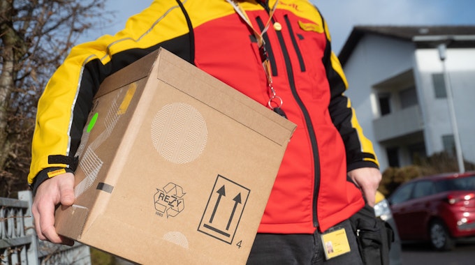 Das Bild zeigt einen DHL-Mitarbeiter mit einem Paket unter seinem Arm.