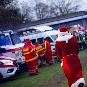 Ein verkleideter Weihnachtsmann inmitten von Einsatzwägen mit Blaulicht an der Kinderklinik des Krankenhauses in Porz