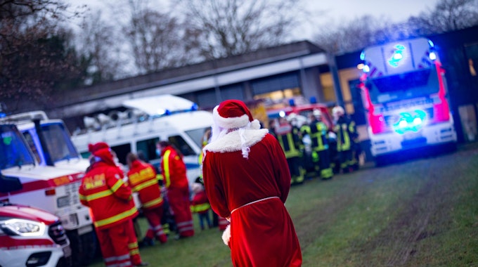 Ein verkleideter Weihnachtsmann inmitten von Einsatzwägen mit Blaulicht an der Kinderklinik des Krankenhauses in Porz